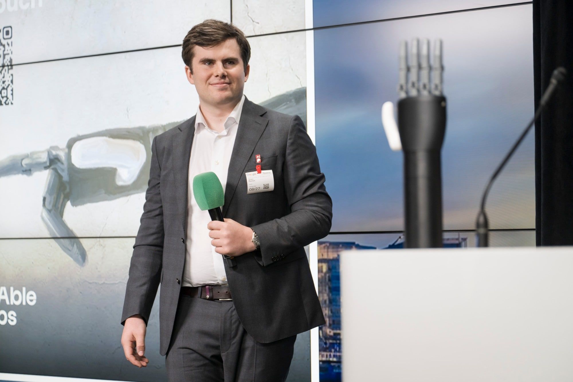 Seán Barrett on stage with a microphone, in front of slides showing a ReAble Labs hand.
